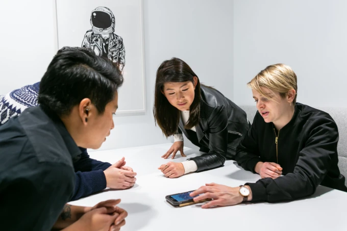 Photo of a group of people hovering a mobile phone on a desk