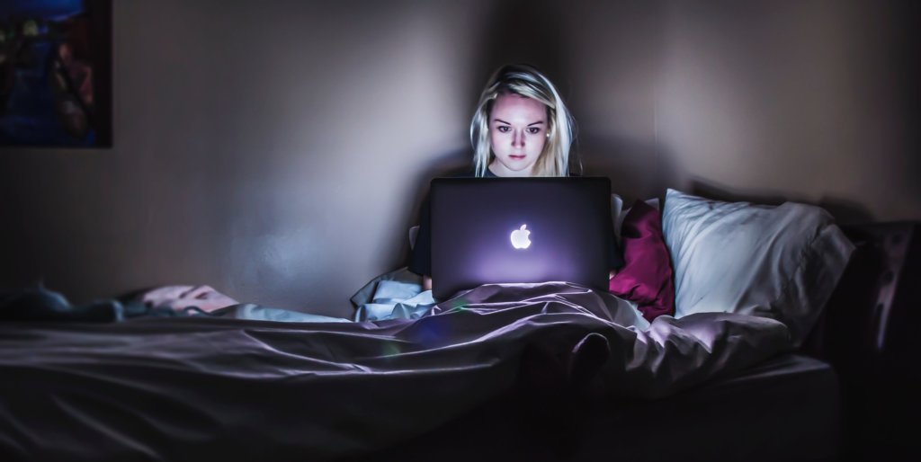 Woman on her bed with laptop browsing fake dating profiles