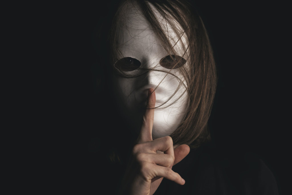 Person in a mask shushing the viewer with the finger.